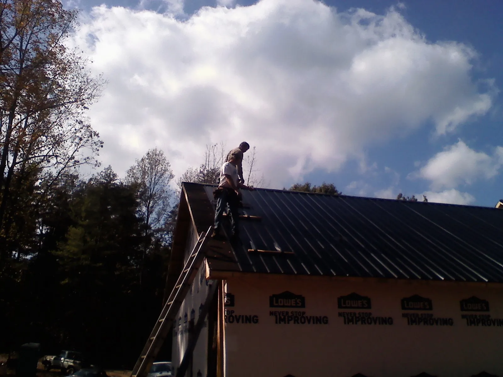 Roofer fastening dark metal panels high against a cloudy sky, from a Roof Inspection job in Milton
